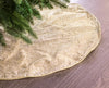 Gold glittery Christmas tree skirt on a wooden floor with a tree branch in the corner.