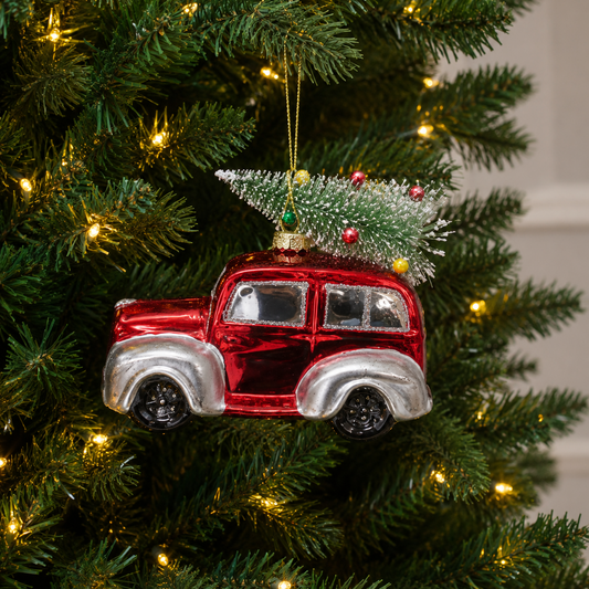 Red and silver vintage car ornament with a small Christmas tree on top, hanging on a decorated tree.