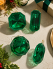 Green crystal Christmas ornaments on a textured surface with festive decorations.