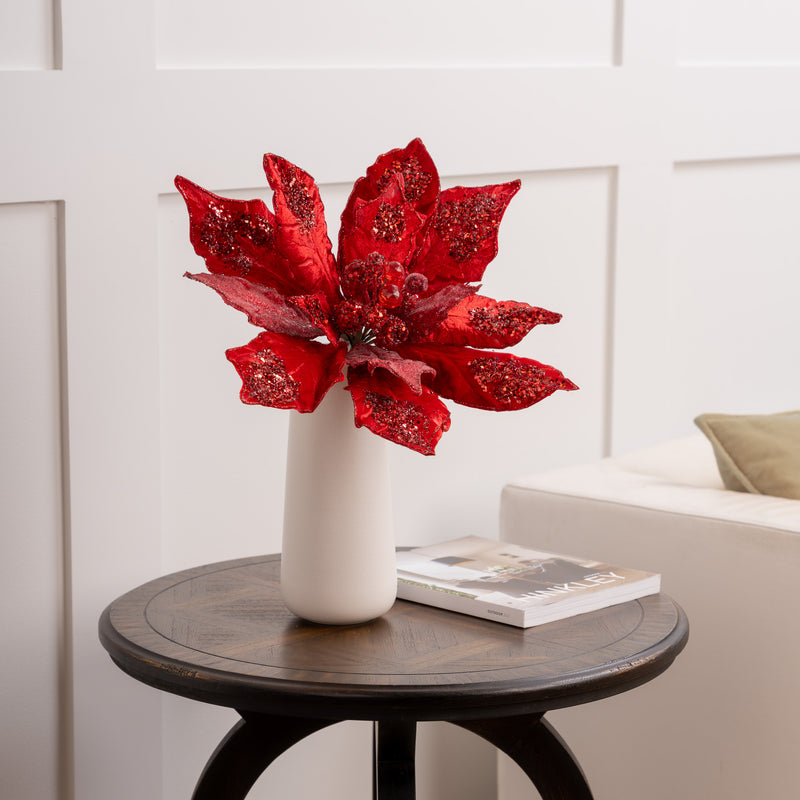 Red poinsettia plant in a white vase on a wooden table with a neutral background