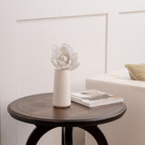 White vase with white glitter flower and book against a neutral wall.
