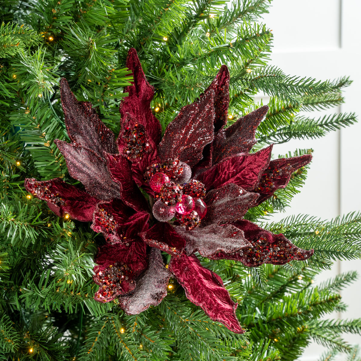 Decorative red flower ornament on a Christmas tree with green branches and lights.