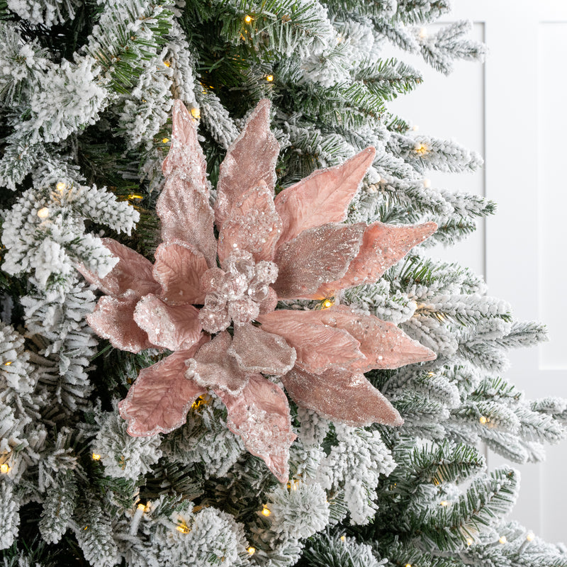 Decorative pink poinsettia on a Christmas tree with white lights.