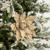 Decorative gold poinsettia on a Christmas tree with snow and lights.