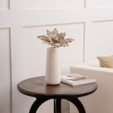 Decorative vase with a unique leaf-shaped object on a wooden table against a white paneled wall.