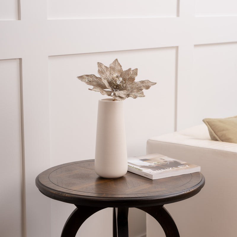Decorative vase with a unique leaf-shaped object on a wooden table against a white paneled wall.