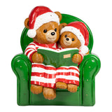 Two teddy bears in Christmas hats sitting on a green chair, reading a book.