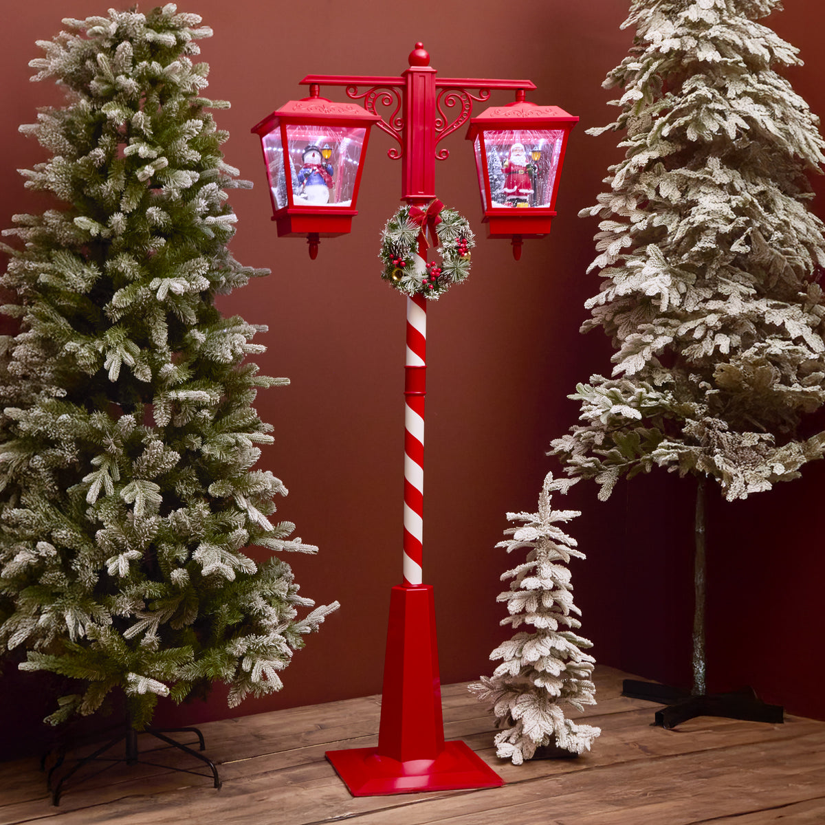 Decorative red and white Christmas lighted pole with candy cane design, surrounded by snow-covered trees.