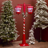 Decorative red and white Christmas lighted pole with candy cane design, surrounded by snow-covered trees.