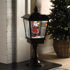 Decorative Christmas lantern with Santa Claus figure inside, next to a Christmas tree.