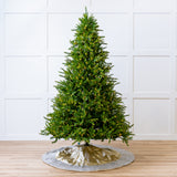 Decorated Christmas tree with lights on a wooden floor against a white paneled wall.