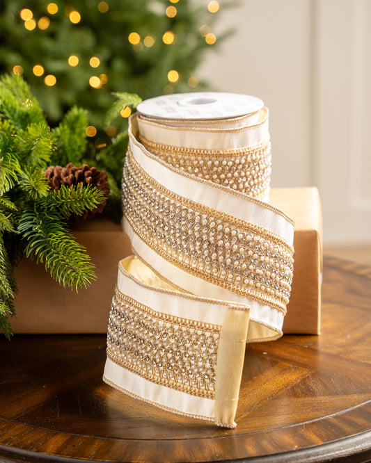 Decorative ribbon with gold and white stripes on a wooden surface with a Christmas tree in the background.