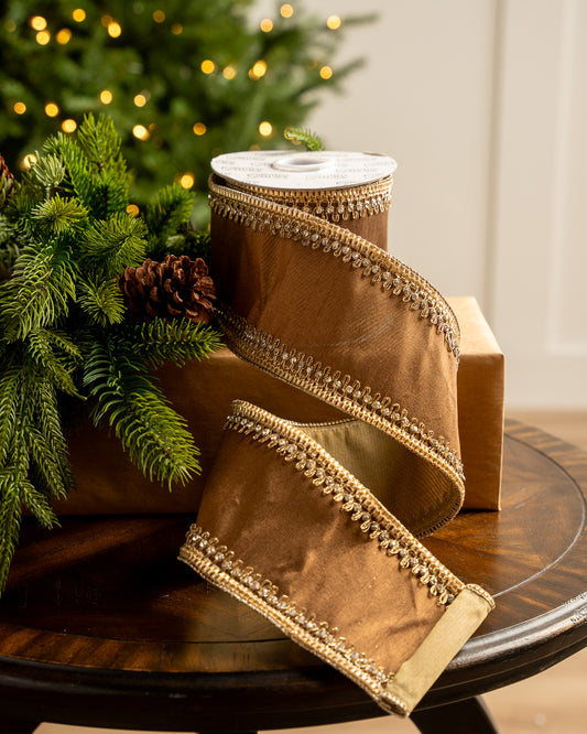 Brown ribbon with gold trim on a wooden table with a Christmas tree in the background