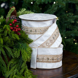 White decorative box with gold ribbon and embellishments on a wooden surface with greenery in the background