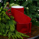 Red glittery ribbons on a table with greenery and pine cones.