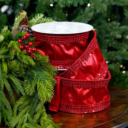 Red satin ribbon with sequins on a wooden surface with green foliage in the background