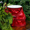 Red satin ribbon with sequins on a wooden surface with green foliage in the background