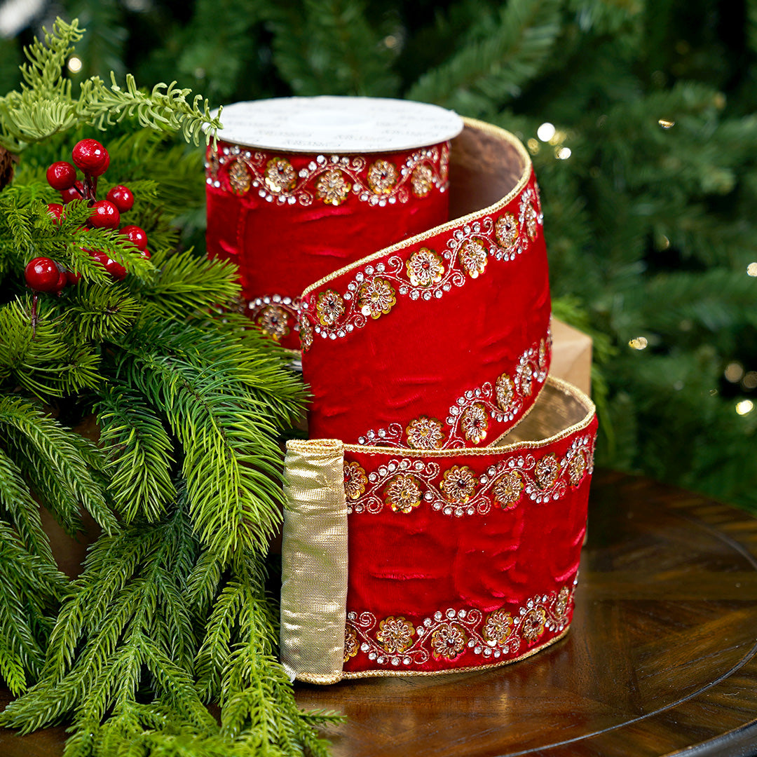 Red ribbon with gold embellishments on a wooden surface with green foliage in the background