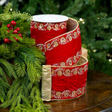 Red ribbon with gold embellishments on a wooden surface with green foliage in the background