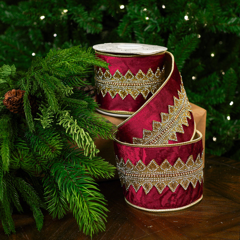 Decorative red ribbon with gold patterns on a wooden surface with green foliage in the background