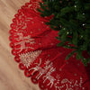 Red Christmas tree skirt with gold reindeer and floral patterns next to a decorated tree on a wooden floor.