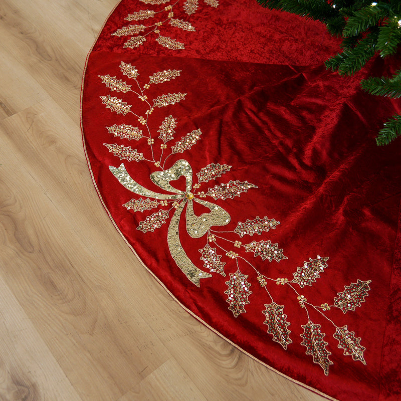 Red Christmas tree skirt with gold embellishments on a wooden floor.