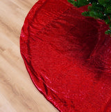 Close-up of a red metallic Christmas tree skirt on a wooden floor.