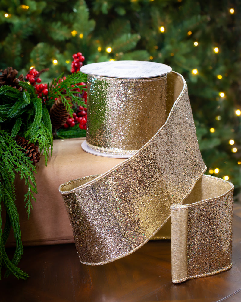 Gold glitter ribbon on a spool with a Christmas tree in the background