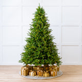 Decorated Christmas tree with gold presents on a wooden floor against a white paneled wall.