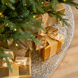 Gold gift boxes with ribbons under a Christmas tree on a decorative tablecloth.