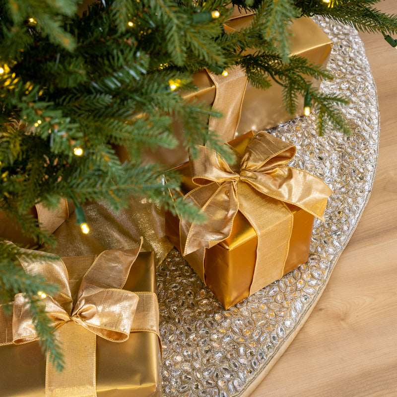 Gold gift boxes with ribbons under a Christmas tree on a decorative tablecloth.