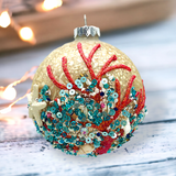 Decorative Christmas ornament with red and green coral-like patterns on a wooden surface.