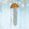 Decorative jellyfish ornament with gold top and sparkling body on a light blue wooden background.