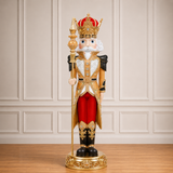 Decorative nutcracker figure with a crown, red outfit, and gold accents on a wooden floor.