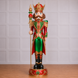 Decorative nutcracker figure with a crown and staff, standing on a wooden floor against a light gray paneled wall.