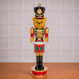 Decorative bear figurine in a nutcracker costume against a light gray wall.