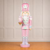 Decorative nutcracker figure in pink and white outfit with a maple leaf hat on a wooden floor.