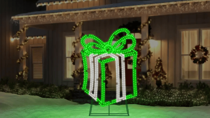 Decorative LED light display of a gift with a bow in front of a house with Christmas decorations.