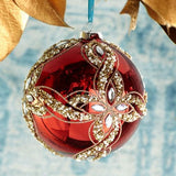 Decorative red Christmas ball ornament with gold embellishments hanging against a textured blue background.