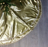Gold metallic Christmas tree skirt on a wooden floor