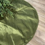Green Christmas tree skirt on a wooden floor with a tree corner.