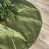 Green Christmas tree skirt on a wooden floor with a tree corner.