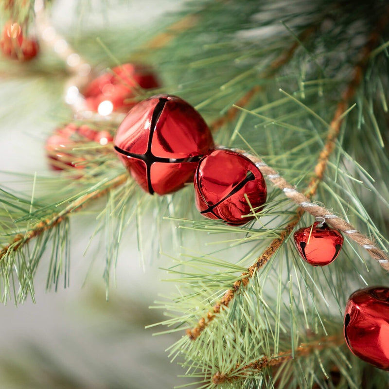 Red jingle bells on a string hanging on a green Christmas tree branch.