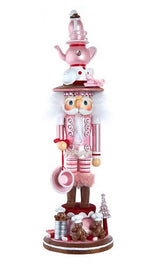 Decorative nutcracker figure in pink and white with a teapot on top, standing on a white background.