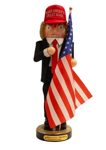 Figurine of a person wearing a red 'Make America Great Again' hat and holding an American flag, with a white background.