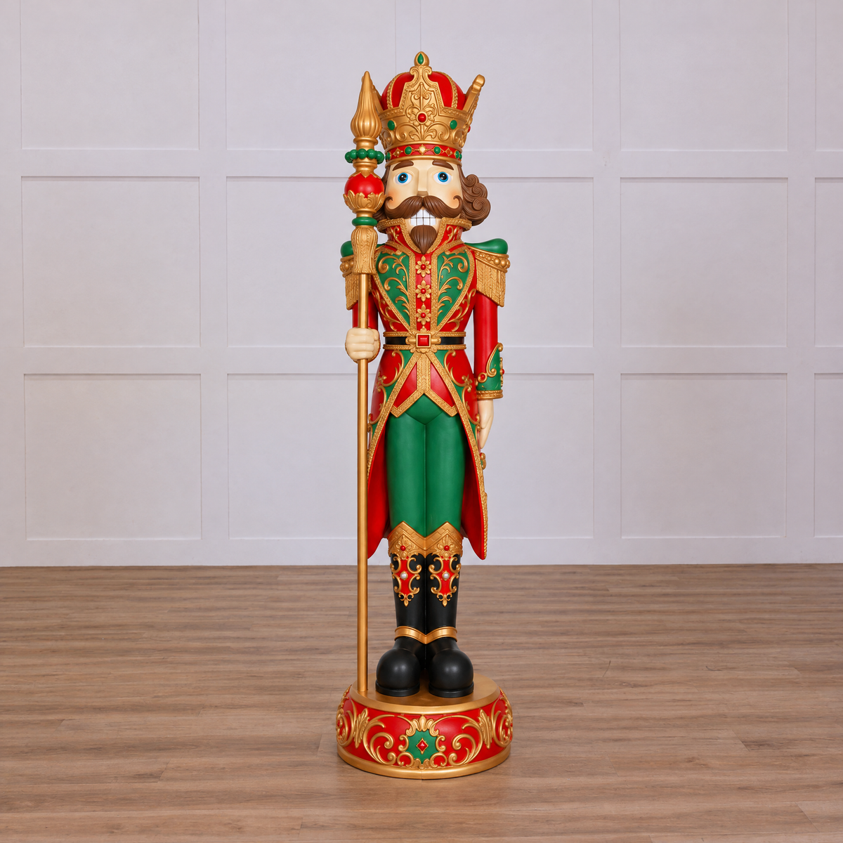 A decorative nutcracker figurine standing on a round base, dressed in a red and green military-style uniform with gold trim, a gold crown, and a gold staff, photographed on a plain white background.