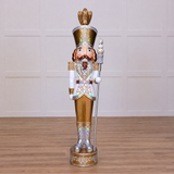 A 8 foot tall Gold and White Nutcracker with warm white LED lights, crafted from fiberglass, with a crown on top and a pose standing.