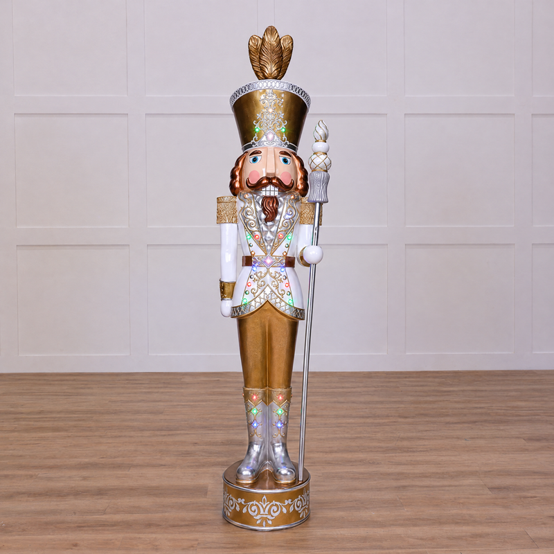 A 8 foot tall Gold and White Nutcracker with warm white LED lights, crafted from fiberglass, with a crown on top and a pose standing.