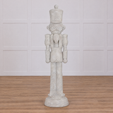A decorative 8 foot tall nutcracker made from resin, designed to look like an antique stone statue, flanked by holiday decorations and displaying a weathered finish.